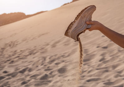 Cropped hand removing sand from shoe at desert
