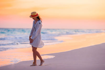 Full length of woman standing on beach against sky during sunset