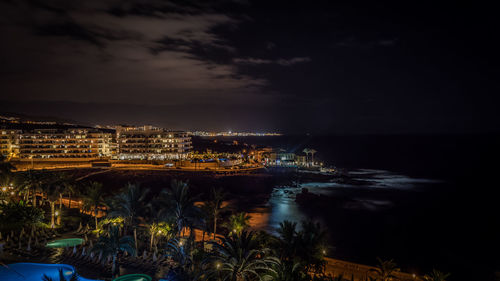 Illuminated cityscape by sea against sky at night