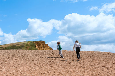 Low angle view of kids walking on sand dune against sky