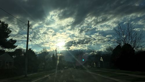 Road by trees against sky during sunset