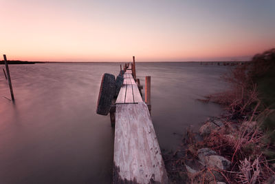 Tires hanging on old wooden jetty over salton sea lake against sky