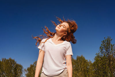 Low angle view of girl tossing hair against sky