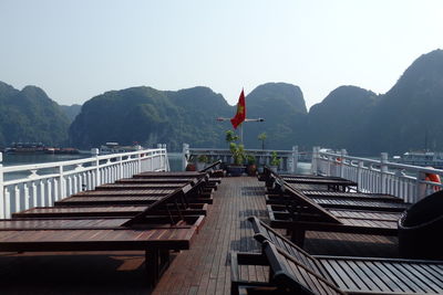 Lounge chairs on pier by mountains against clear sky