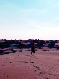 Rear view of woman walking at beach against sky