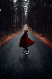 Rear view of woman walking on road in forest