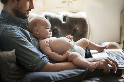 Cropped image of man using laptop computer while sitting with son at home