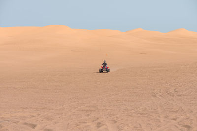 Man riding quadbike in desert against clear sky