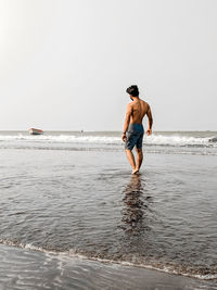 Rear view of shirtless man standing on beach against clear sky