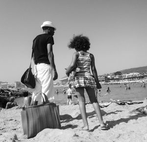 Rear view of father and daughter standing on sand at beach against clear sky