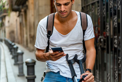 Young latin man with crutches and mobile in the street