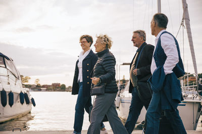 Senior male and female friends walking on pier against sky