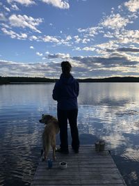 Rear view of woman with dog on lake against sky