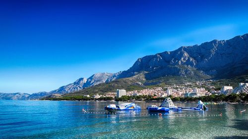 Boats moored on sea by mountains against clear blue sky