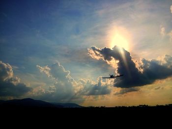 Airplane flying over silhouette field against sky during sunset