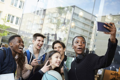 Teenage girl taking selfie with friends by store in city