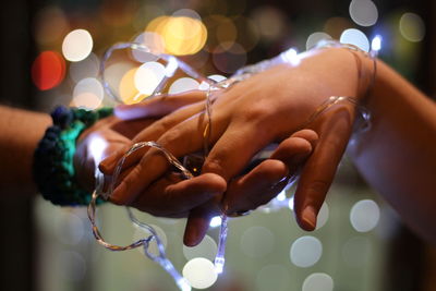 Close-up of woman hand holding illuminated christmas lights at night