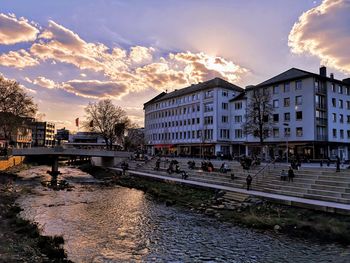 Arch bridge over river amidst buildings in city against sky