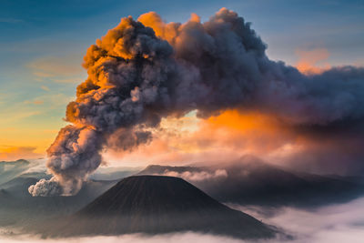 Smoke emitting from volcanic mountain against sky during sunset