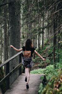 Rear view of woman running on footbridge in forest