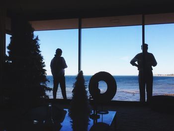 Rear view of silhouette man standing by window against sky