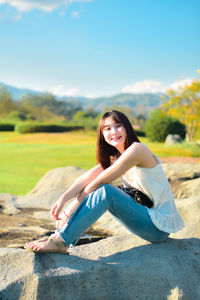 Young woman sitting on field against sky