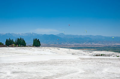 Paragliders flying above white travertines of pamukkale in an ancient city of hierapolis in turkey.