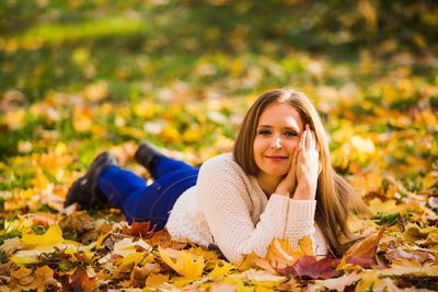 Portrait of smiling woman lying down leaves during autumn