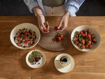 Woman's hands prepares oatmeal for breakfast with strawberries in the kitchen. view from above.