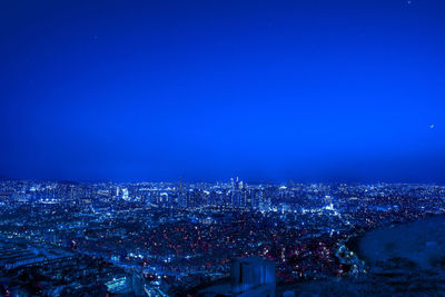 High angle view of illuminated cityscape against clear blue sky