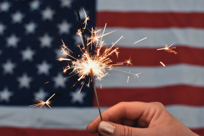 Cropped hand holding sparkler in front of usa flag 