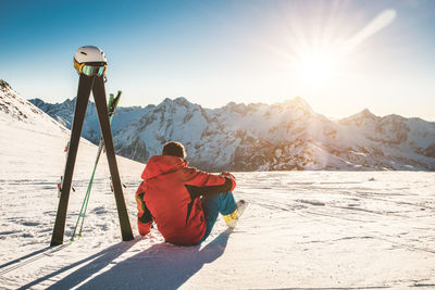 Rear view of man sitting on snowcapped mountain against sky