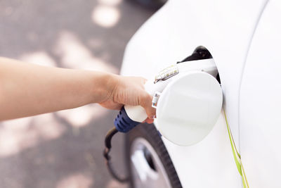 Cropped hand of woman charging electric car at station