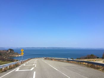 Road by sea against clear blue sky