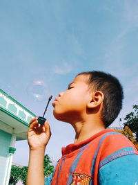 Low angle view of boy blowing bubble against sky during sunny day