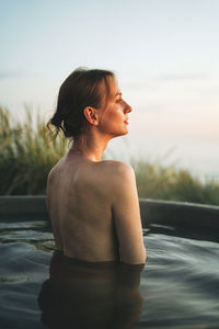 Side view of shirtless woman standing against sky