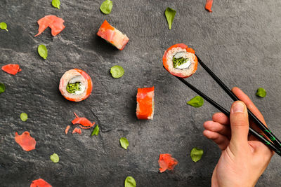 Cropped image of hand holding sushi with chopsticks on stone tray