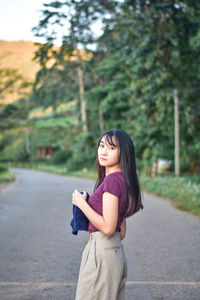 Portrait of woman standing on road against tree