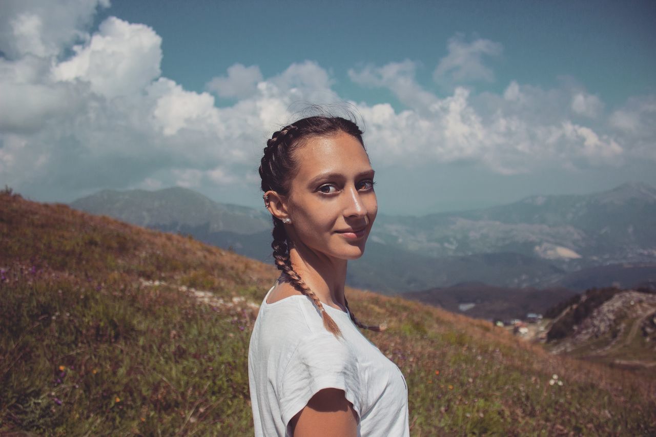 one person, mountain, sky, leisure activity, lifestyles, cloud - sky, young adult, real people, standing, portrait, scenics - nature, nature, beauty in nature, landscape, young women, tranquility, mountain range, non-urban scene, day, outdoors, beautiful woman, hairstyle