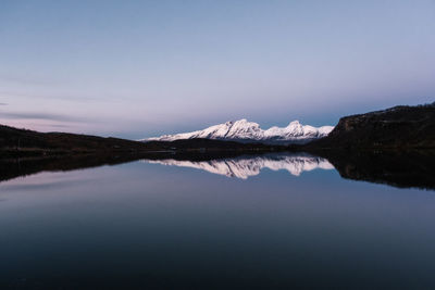 Snowcapped mountains reflecting in a clear lake after sunset