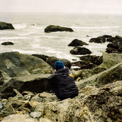 Rear view of man sitting on rocks at beach