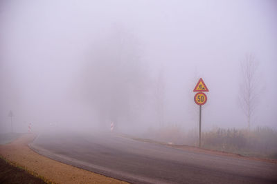 Road sign by trees against sky during foggy weather