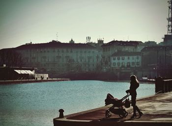 Side view of man sitting on riverbank against clear sky