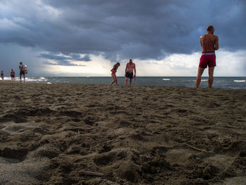 Full length of shirtless man standing at beach against sky