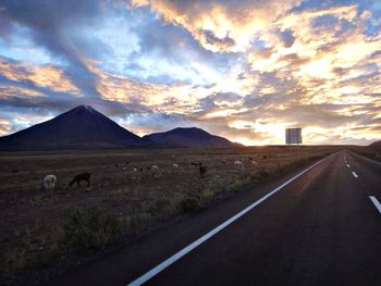 Road passing through field against cloudy sky