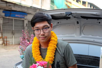 Portrait of young man wearing flowers at car trunk