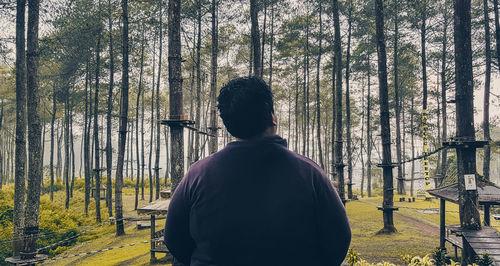 Rear view of man standing by trees in forest