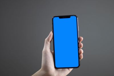 Close-up of hand holding smart phone against blue background