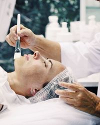 Cropped hands on cosmetologist applying cream on female customer chin