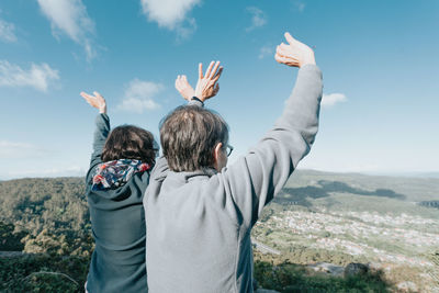 Rear view of man with arms raised against sky